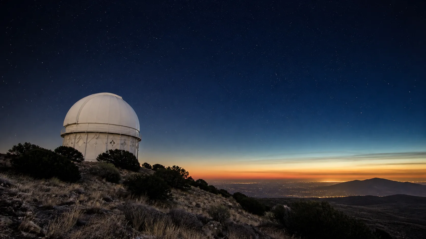 A white observatory dome beneath the darkening West Texas sky and distant city glow